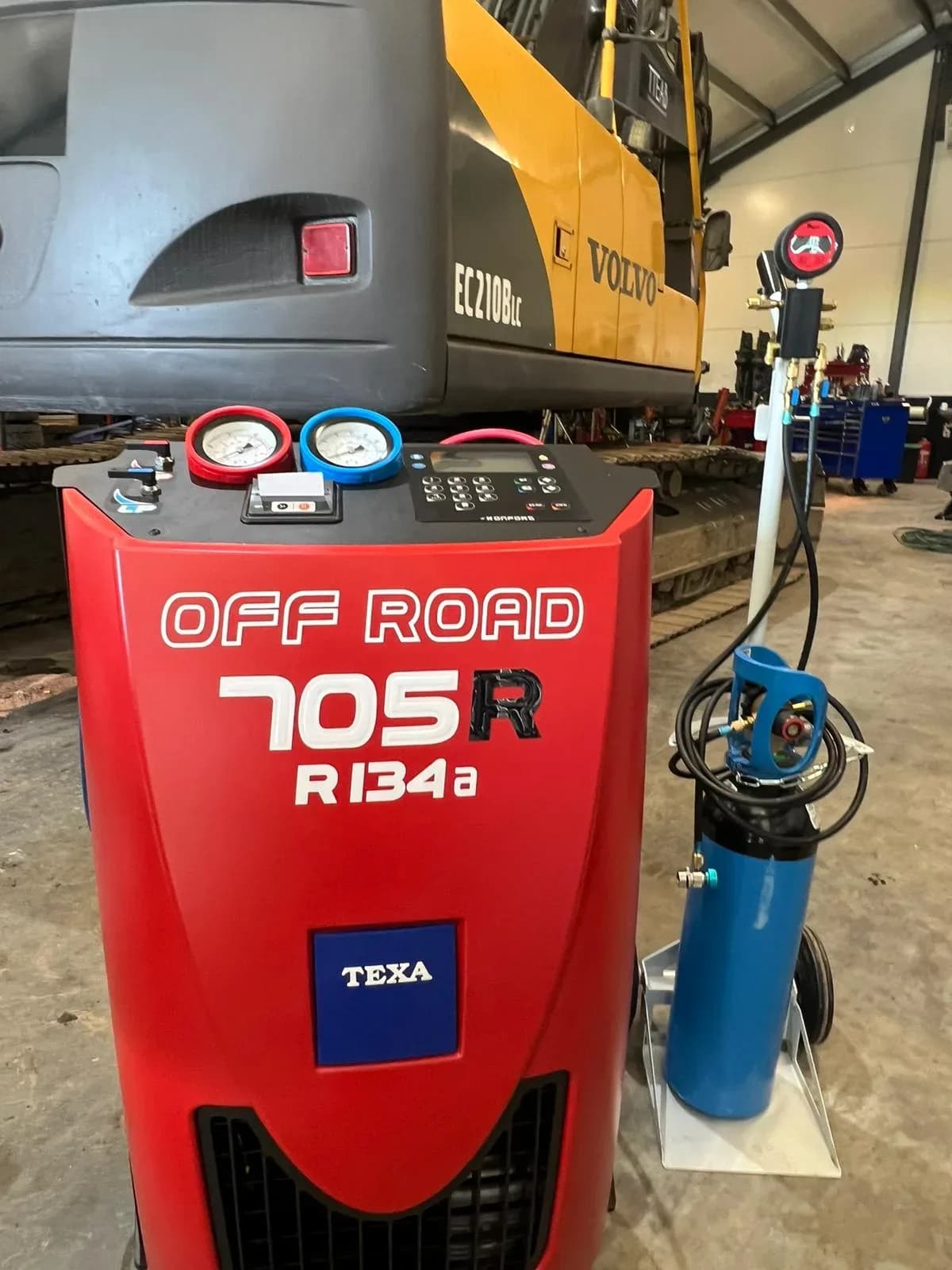 Volvo grävmaskin i verkstaden med en röd TEXA Off Road 705R AC-servicemaskin