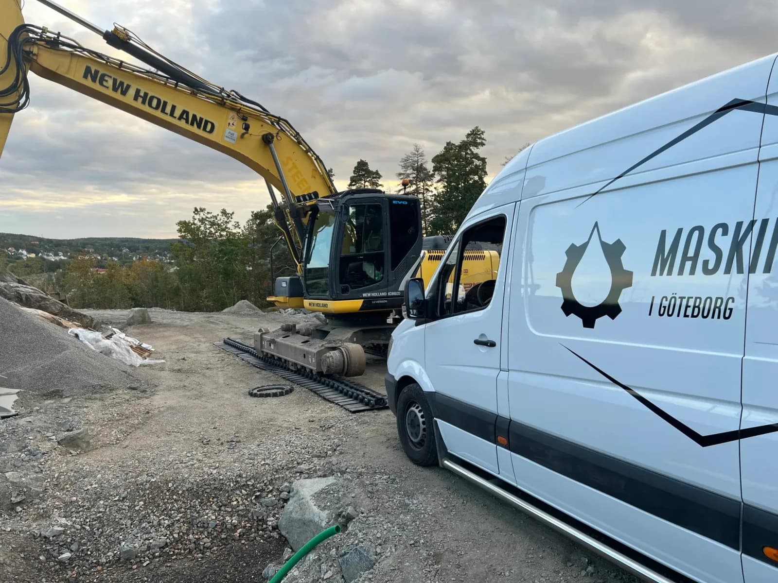 New Holland-grävmaskin och vit servicebil från Maskinservice i Göteborg på en byggarbetsplats