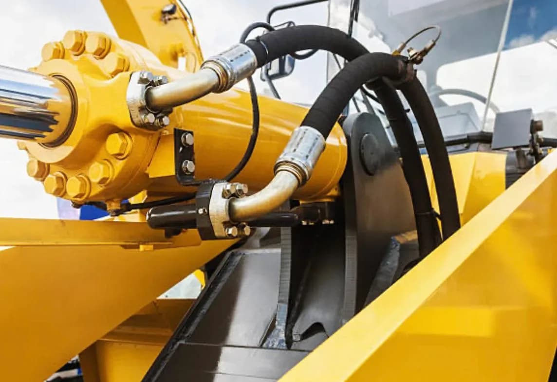 Hydraulcylinder och hydraulslangar på gul entreprenadmaskin
